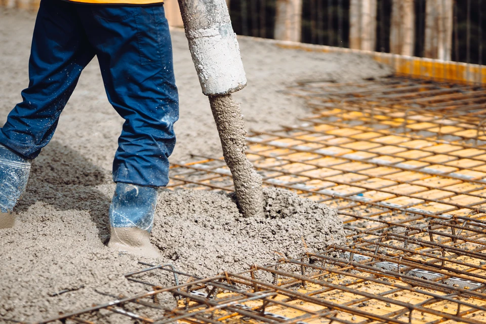 Chantier de construction en ext&eacute;rieur avec ouvrier en combinaison bleue coulant du b&eacute;ton liquide via une goulotte sur ferraillage
