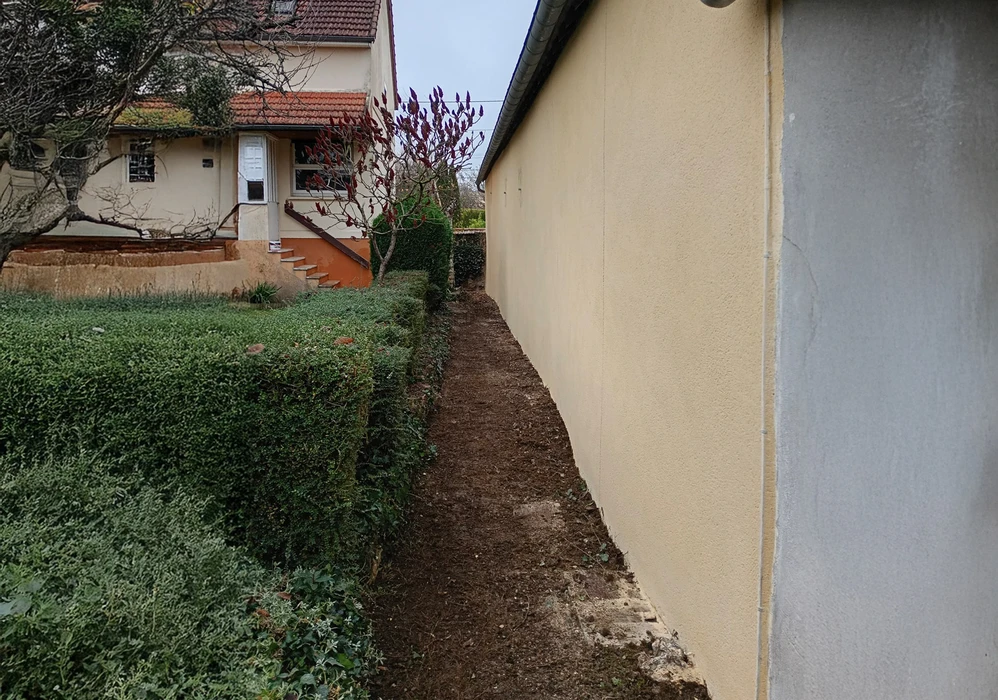 Extérieur résidentiel avec mur de clôture beige partiellement peint, zone de travaux de rénovation