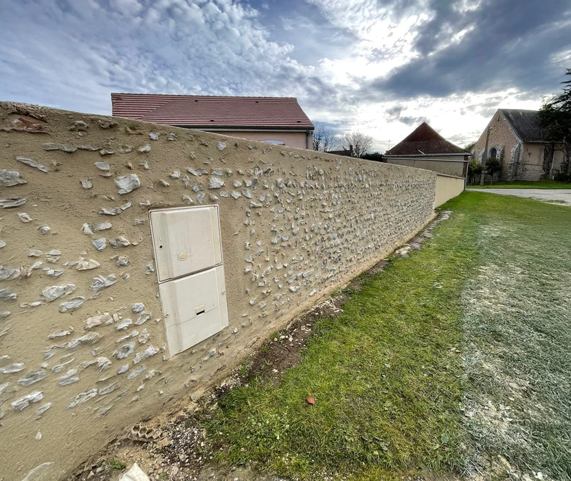 Mur en pierre et silex traditionnel avec enduit terre, intégrant un coffret électrique encastré