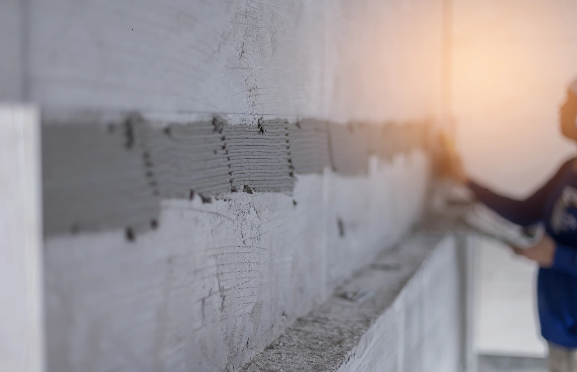 Chantier de construction ext&eacute;rieur avec ouvrier en casque blanc maniant une pelle pr&egrave;s d'une b&eacute;tonni&egrave;re