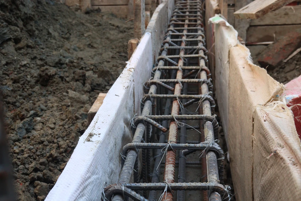 Ouvrier en vêtements de travail rouge et pantalon gris verse du béton liquide depuis une benne sur chantier extérieur