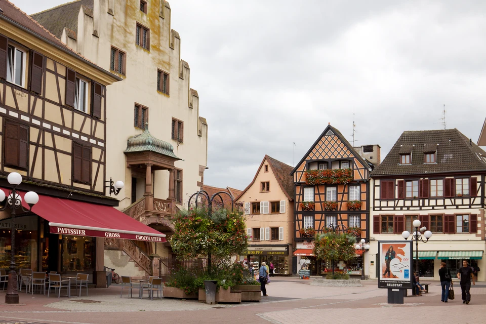 Maisons alsaciennes traditionnelles à colombages avec façades en bois et crépi, volets colorés bleus et rouges, toitures en tuiles d'argile orange